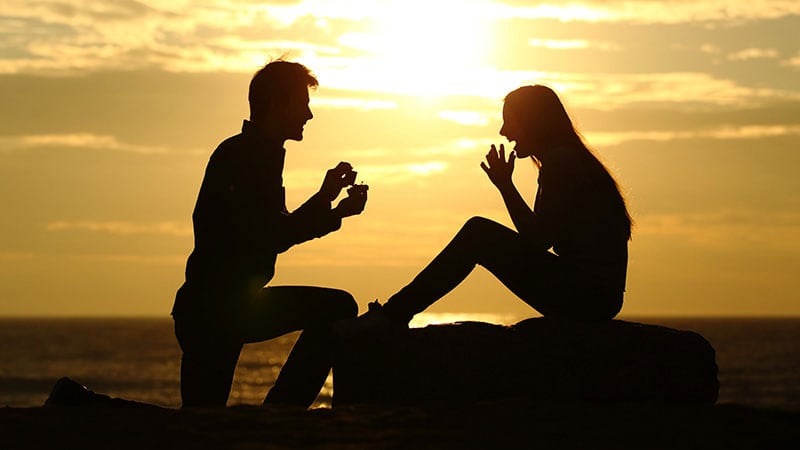 海に沈む夕日と恋人からプロポーズを受ける女性